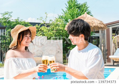 Couple toasting with beer glasses by the pool at a vacation resort hotel Couple toasting with beer glasses by the pool at a vacation resort hotel 139734373