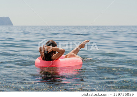 Woman floating tube young lady relaxing on a pink inner tube in the clear blue sea with horizon and copy space Woman floating tube young lady relaxing on a pink inner tube in the clear blue sea with horizon and copy space 139736089