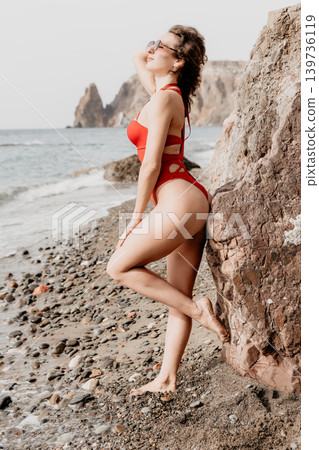 Woman beach swimsuit posing against rocks on a scenic coastline with ocean waves during a relaxing summer vacation 139736119