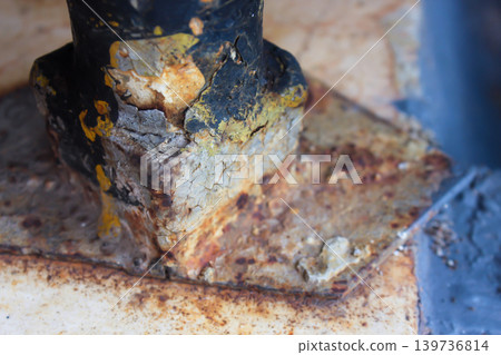 Detailed close-up photo of a rusty metal structure base with peeling paint, corrosion, and weathered industrial texture.  139736814