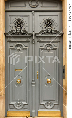 Ornate grey door of a classical parisian building with carved lions, fancy wrought iron grilles, and shiny golden hardware 139737297