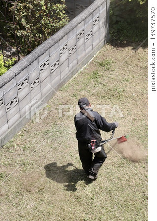 A middle-aged man mowing the lawn with a gasoline-powered brush cutter. A middle-aged man mowing the lawn with a gasoline-powered brush cutter. 139737570