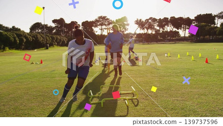 Training women in white jerseys, blue shorts navigating low hurdles on grass at sunset with cones Training women in white jerseys, blue shorts navigating low hurdles on grass at sunset with cones 139737596