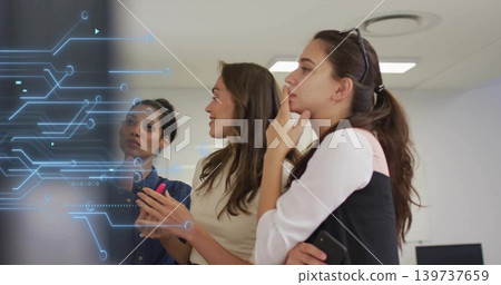 Reviewing three women wearing blouses at meeting room glass display with circuit overlay and phone Reviewing three women wearing blouses at meeting room glass display with circuit overlay and phone 139737659