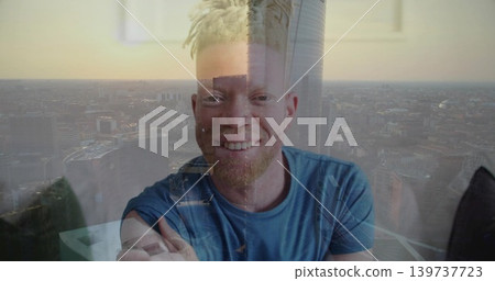 Smiling man with blond dreads and beard wearing blue tee leaning in flat with skyline reflection Smiling man with blond dreads and beard wearing blue tee leaning in flat with skyline reflection 139737723