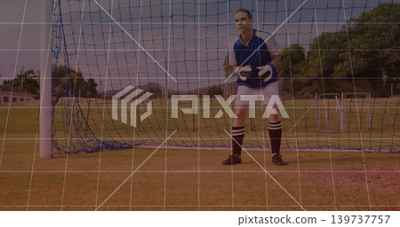 Standing female goalkeeper wearing navy jersey and goalkeeper gloves in goal on grass, copy space 139737757