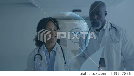 Reviewing two doctors studying charts at clinic, wearing lab coats stethoscope phone hologram globe Reviewing two doctors studying charts at clinic, wearing lab coats stethoscope phone hologram globe 139737856