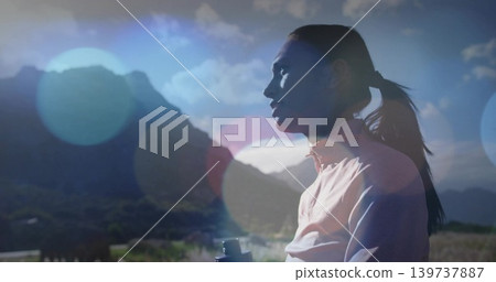 Standing woman in light jacket, ponytail watching peaks with binoculars amid lens flare, copy space 139737887