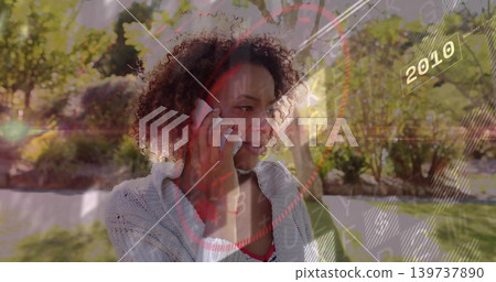 Holding smartphone, woman in cardigan and red top talking in sunlit garden with HUD 2010 graphics Holding smartphone, woman in cardigan and red top talking in sunlit garden with HUD 2010 graphics 139737890