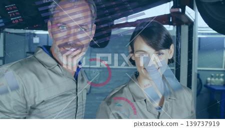 Standing two technicians wearing light-gray coveralls reviewing HUD data in service bay with lift Standing two technicians wearing light-gray coveralls reviewing HUD data in service bay with lift 139737919