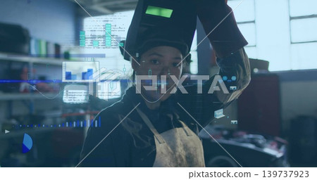 Lifting welding helmet, woman welder wearing leather apron standing at garage bay with AR overlays Lifting welding helmet, woman welder wearing leather apron standing at garage bay with AR overlays 139737923