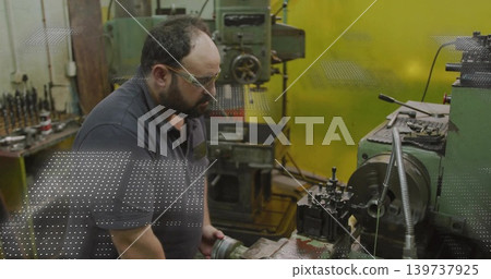 Turning machinist leaning over lathe chuck in machine shop, wearing safety glasses and polo 139737925