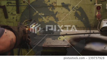 Holding gloved arm aiming blowtorch at metal on workshop bench, welding helmet visible, copy space 139737928
