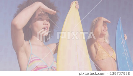 Standing two women shielding eyes at beach, holding surfboards, wearing bikinis and headband Standing two women shielding eyes at beach, holding surfboards, wearing bikinis and headband 139737958