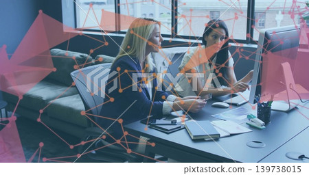 Collaborating two mature women in business casual reviewing papers at desk, with monitor overlay Collaborating two mature women in business casual reviewing papers at desk, with monitor overlay 139738015
