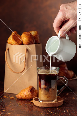 Coffee latte and paper bag with croissants on a brown background. Coffee latte and paper bag with croissants on a brown background. 139738124