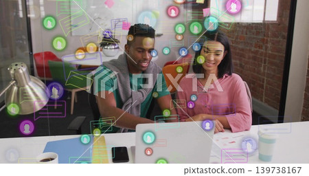Collaborating man green tee and woman pink blouse reviewing laptop, paper charts, AR icons at desk Collaborating man green tee and woman pink blouse reviewing laptop, paper charts, AR icons at desk 139738167
