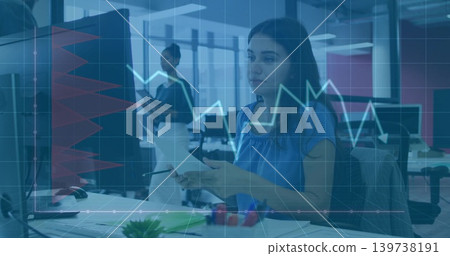 Working woman in blue blouse reviewing files at open office with financial overlay monitor, tablet Working woman in blue blouse reviewing files at open office with financial overlay monitor, tablet 139738191