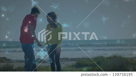 Pointing couple in red T-shirt and yellow sweater examining ground on coastal dune, blue holograms Pointing couple in red T-shirt and yellow sweater examining ground on coastal dune, blue holograms 139738195