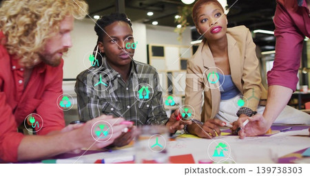 Leaning woman in tan blazer and colleagues discussing plan at modern office, with green AR icons Leaning woman in tan blazer and colleagues discussing plan at modern office, with green AR icons 139738303
