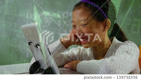 Smiling girl whiteknit purpleband using tablet on stand at table with green stock data, copy space Smiling girl whiteknit purpleband using tablet on stand at table with green stock data, copy space 139738356