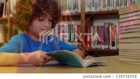 Reading boy in bright-blue shirt at library table, holding light-blue book, hardcover stack nearby Reading boy in bright-blue shirt at library table, holding light-blue book, hardcover stack nearby 139738358