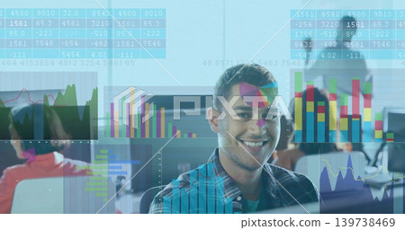 Smiling man in plaid shirt sitting at open-plan office desk, viewing translucent charts on monitors Smiling man in plaid shirt sitting at open-plan office desk, viewing translucent charts on monitors 139738469