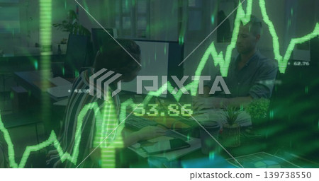 Typing woman in striped blouse using keyboard and tablet at office desk, showing green charts 139738550