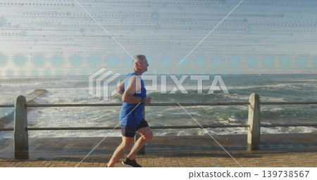 Jogging senior man in blue sleeveless top and black shorts along seafront path with railing, watch Jogging senior man in blue sleeveless top and black shorts along seafront path with railing, watch 139738567