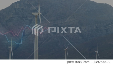 Towering white 3-blade wind turbine centered on slope, showing rocky mountain and blue-pink graph 139738699
