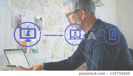 Working senior man wearing glasses, dark sweater using laptop, tablet in home office, network icons Working senior man wearing glasses, dark sweater using laptop, tablet in home office, network icons 139738889