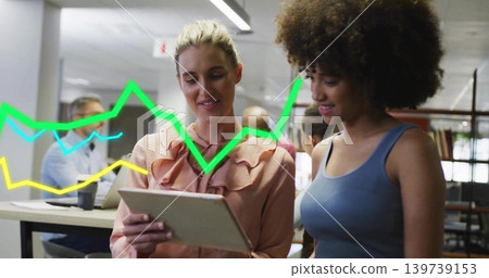 Reviewing tablet, two women wearing peach blouse and blue top in open office with line graphs Reviewing tablet, two women wearing peach blouse and blue top in open office with line graphs 139739153