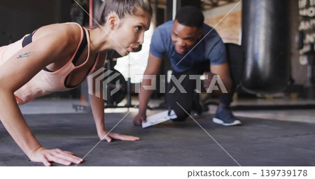 Doing push-up client wearing pink bra, dark leggings on rubber floor, trainer coaching, clipboard Doing push-up client wearing pink bra, dark leggings on rubber floor, trainer coaching, clipboard 139739178