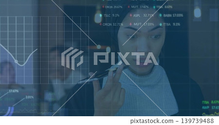 Studying woman in turtleneck and blazer holding pen in office, glass display with financial charts Studying woman in turtleneck and blazer holding pen in office, glass display with financial charts 139739488