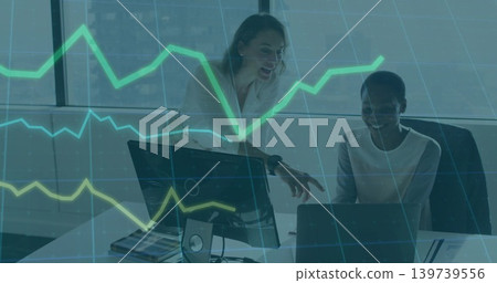Pointing two women working in office in blazers, using laptop and screen with green-yellow chart Pointing two women working in office in blazers, using laptop and screen with green-yellow chart 139739556