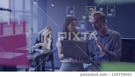 Holding laptop, coworkers in business attire gesturing and explaining screen in office with charts Holding laptop, coworkers in business attire gesturing and explaining screen in office with charts 139739562