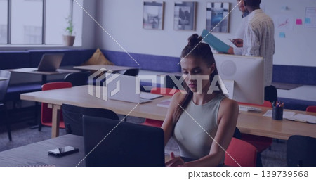 Working woman in sleeveless top with top knot typing on laptop at co-working space, with smartphone Working woman in sleeveless top with top knot typing on laptop at co-working space, with smartphone 139739568