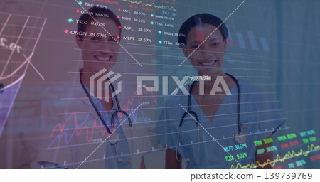 Standing nurses in scrubs viewing finance charts on glass panel in clinic, with tablet, stethoscope 139739769