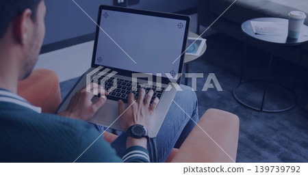 Typing man wearing green sweater on orange armchair in lounge, with laptop corner marks, copy space Typing man wearing green sweater on orange armchair in lounge, with laptop corner marks, copy space 139739792