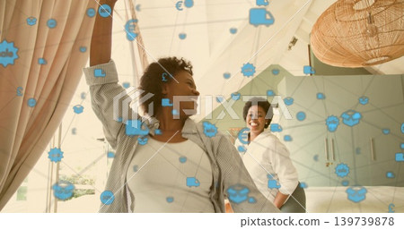 Smiling two mid adult Black women wearing white tops standing in bright bedroom, with blue icons Smiling two mid adult Black women wearing white tops standing in bright bedroom, with blue icons 139739878
