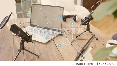 Showing podcast setup occupying center on wood table by window, with laptop and microphones Showing podcast setup occupying center on wood table by window, with laptop and microphones 139739880