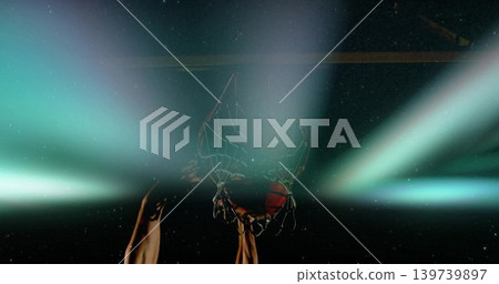 Gripping bare muscular male arms pulling rim while basketball passing through net in arena, lights Gripping bare muscular male arms pulling rim while basketball passing through net in arena, lights 139739897
