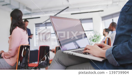Typing woman in denim jacket using silver laptop on lap in workshop, flip chart, copy space Typing woman in denim jacket using silver laptop on lap in workshop, flip chart, copy space 139739904