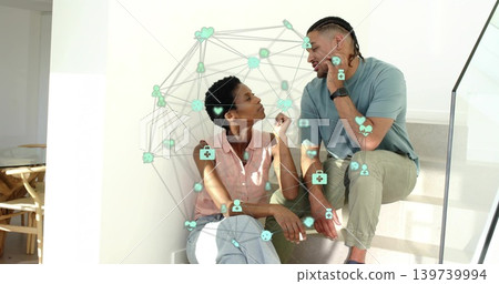 Sitting couple home stairs talking, woman in pink top and jeans, man adjusting earbud, teal overlay Sitting couple home stairs talking, woman in pink top and jeans, man adjusting earbud, teal overlay 139739994