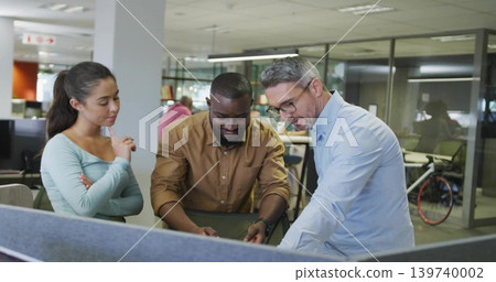 Pointing man and colleagues in office shirts leaning over desk in open office with bicycle Pointing man and colleagues in office shirts leaning over desk in open office with bicycle 139740002