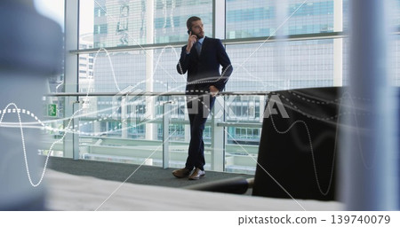 Leaning executive holding smartphone to ear in atrium, in suit and tie, glass windows with waveform Leaning executive holding smartphone to ear in atrium, in suit and tie, glass windows with waveform 139740079