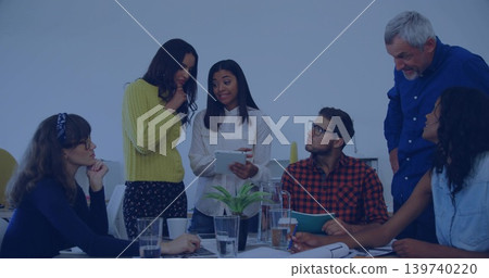 Presenting woman in yellow top holding tablet, team reviewing papers at meeting table with plant Presenting woman in yellow top holding tablet, team reviewing papers at meeting table with plant 139740220