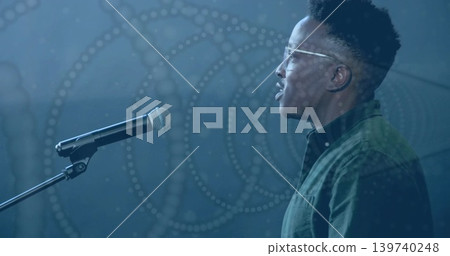 Singing man in clear specs green-collared facing mic on stand in studio dotted pattern, copy space Singing man in clear specs green-collared facing mic on stand in studio dotted pattern, copy space 139740248