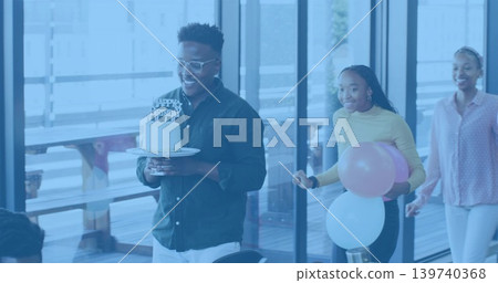 Walking male colleague wearing dark shirt carrying two-tier birthday cake in office, with balloons Walking male colleague wearing dark shirt carrying two-tier birthday cake in office, with balloons 139740368