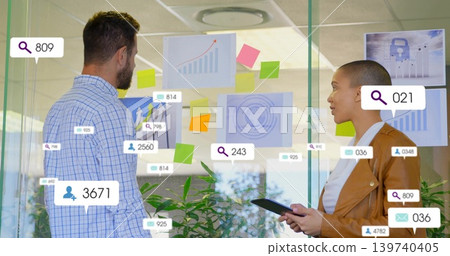 Standing two staff in suits studying glass charts at office, holding tablet, pointing at AR icons 139740405